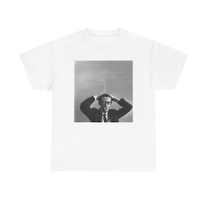May include: White t-shirt with a black and white image of a man in a suit, glasses, and a tie, with his hands on his head. The image has a vintage, artistic aesthetic.