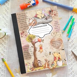 May include: Composition book featuring Winnie the Pooh and friends with inspirational quotes. The cover has a black spine and a decorative floral and tree design. Includes the text "COMPOSITION BOOK".