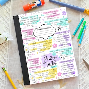 May include: A composition notebook with a black spine and a white cover adorned with colorful text and floral designs. The cover features the phrase "The Power of Faith" and various Bible verses.