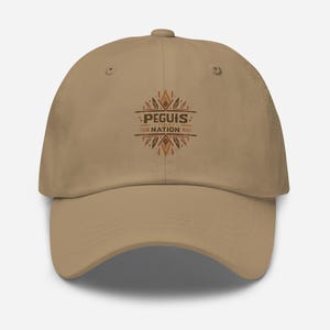 May include: A tan baseball cap with the text "PEGUIS NATION" in a brown, decorative font. The cap has a curved brim and an adjustable strap. The design includes feather-like shapes.