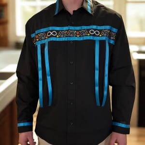 Puede incluir: Camisa negra abotonada con mangas largas. La camisa presenta cintas turquesas y detalles bordados en el pecho y en el cuello. El diseño incluye símbolos de infinito y motivos florales.