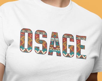 May include: White t-shirt with the word "OSAGE" in a colorful, patterned design. The design incorporates shades of red, blue, orange, and white, creating a vibrant and eye-catching look. The shirt is a simple crew neck style.