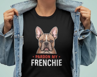 May include: Black t-shirt featuring a detailed illustration of a French Bulldog's face. The text "Pardon My Frenchie" is printed below the dog image in white, with red star accents. The person is wearing a denim jacket.