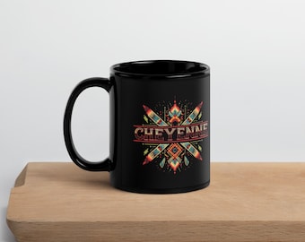 May include: Black ceramic mug with the word "CHEYENNE" in a red, orange, and teal design. The mug has a handle and is sitting on a wooden surface.