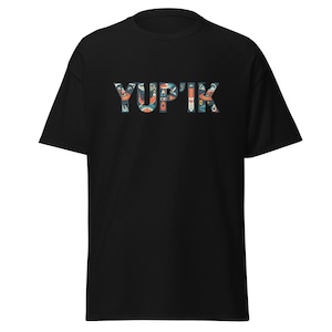 May include: Black t-shirt with the word "YUPIK" in a colorful, patterned design. The letters are filled with various shapes and colors, including orange, blue, and white. The shirt is a classic crew neck style.