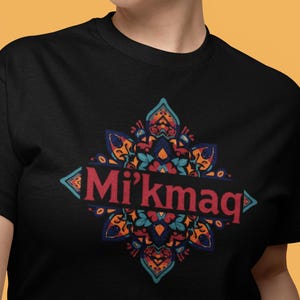 Peut inclure: T-shirt noir avec un motif symétrique coloré. Le design présente le mot "Mi'kmaq" en rouge, entouré de motifs floraux et géométriques turquoise, orange et bleus. Un graphisme saisissant et coloré.