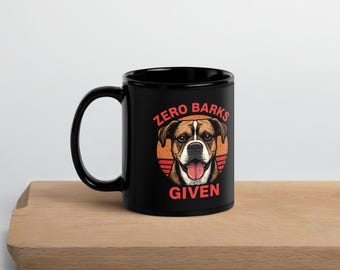 May include: Black ceramic mug with a dog graphic and the text "Zero Barks Given." The dog illustration features a brown and white dog with its tongue out, set against an orange and red background. The mug is on a wooden surface.