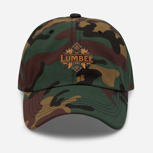 Könnte beinhalten: Tarnfarbene Baseballkappe mit dem Wort "LUMBER" in Orange und einem geometrischen Design. Die Kappe ist in Grün-, Braun- und Schwarztönen gehalten.