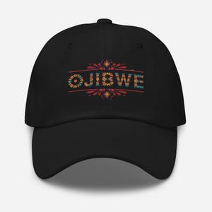 Könnte beinhalten: Schwarze Baseballkappe mit dem Wort "OJIBWE" in bunten, gemusterten Buchstaben. Der Text ist mittig auf der Vorderseite der Kappe platziert, über einem dekorativen Design. Die Kappe hat einen gebogenen Schirm.