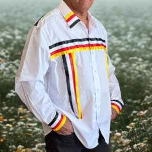May include: A white long-sleeve button-down shirt featuring horizontal and vertical ribbon trim in black, red, and yellow. The shirt has a classic collar, a buttoned front placket, and matching ribbon detailing on the cuffs and collar points.