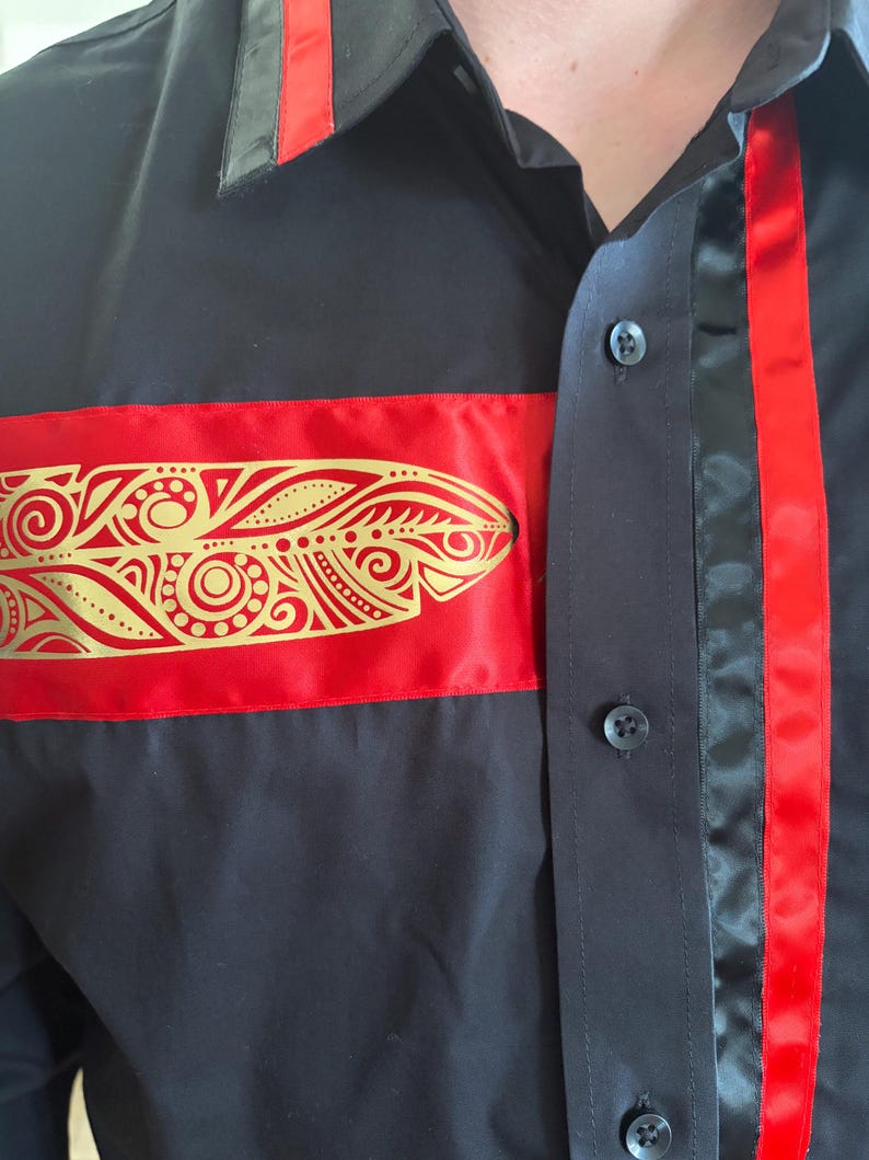 May include: A black button-down shirt featuring a horizontal red satin band across the chest adorned with a gold metallic feather-shaped print. The shirt includes a vertical red satin stripe along the button placket and a red accent on the collar.