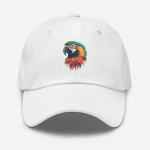 Könnte beinhalten: Weiße Baseballkappe mit einer bunten Papageien-Illustration. Der Papagei hat grüne, blaue, orange und gelbe Federn. Die Kappe ist aus einem weichen Material und hat einen gebogenen Schirm.