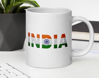 Op de afbeelding: Witte keramische mok met het woord "INDIA" in oranje, wit, groen en rood, met het ontwerp van de Indiase vlag. De mok heeft een gebogen handvat en staat op een wit oppervlak.