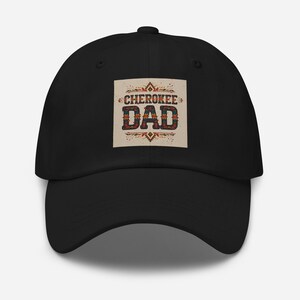 May include: Black baseball cap with the text "CHEROKEE DAD" in a square patch. The text is in a decorative font with a Native American-inspired design. The cap is a classic six-panel design with a curved brim.