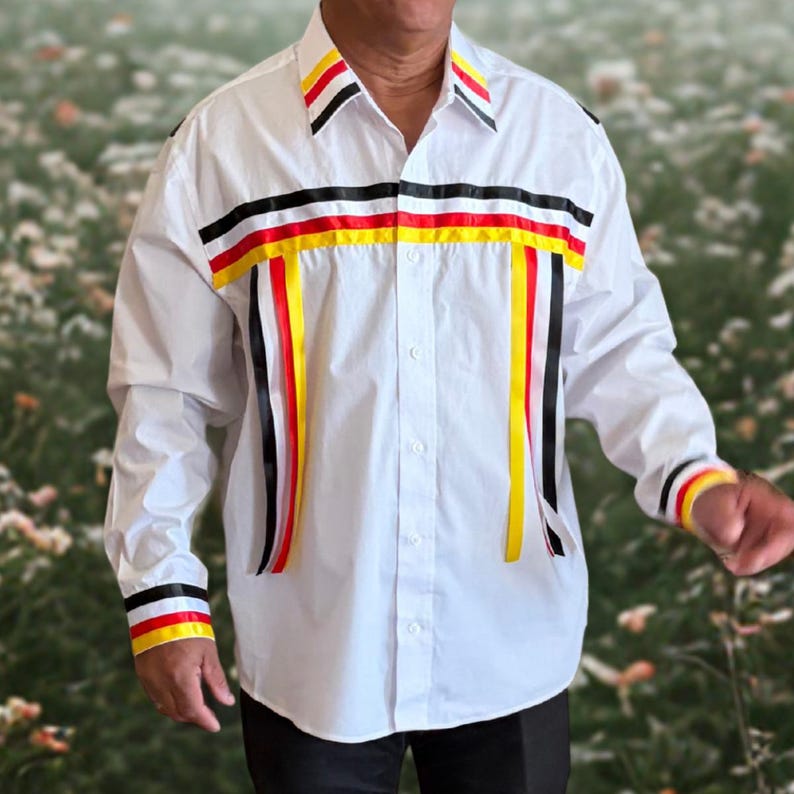 May include: A white long-sleeve button-down shirt featuring horizontal and vertical ribbon trim in black, red, and yellow. The collar, cuffs, and chest area are decorated with these colorful ribbons, creating a structured, layered appearance.