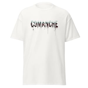 May include: White t-shirt with the word "COMANCHE" printed across the chest. The text is in a distressed style, with a gradient of colors and dripping effects. The shirt has short sleeves and a crew neck.
