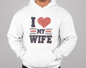 May include: A white hooded sweatshirt featuring a graphic print on the chest. The design includes a distressed red heart and the dark blue text I LOVE MY WIFE, with the word MY centered between two horizontal red and blue striped bars.