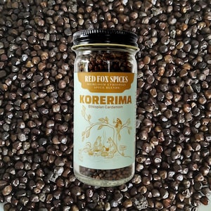 Può includere: Un barattolo di vetro di cardamomo etiope, etichettato "Korerima" da Red Fox Spices. Il barattolo è pieno di semi marrone scuro e poggia su un letto di semi simili. L'etichetta presenta un'illustrazione di una volpe.