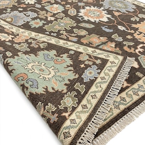 Peut inclure: Tapis marron fonc&eacute; avec un motif floral complexe dans des tons de bleu, vert et p&ecirc;che. Le tapis a une bordure cr&egrave;me et une frange. Le design est de style traditionnel, id&eacute;al pour un salon.