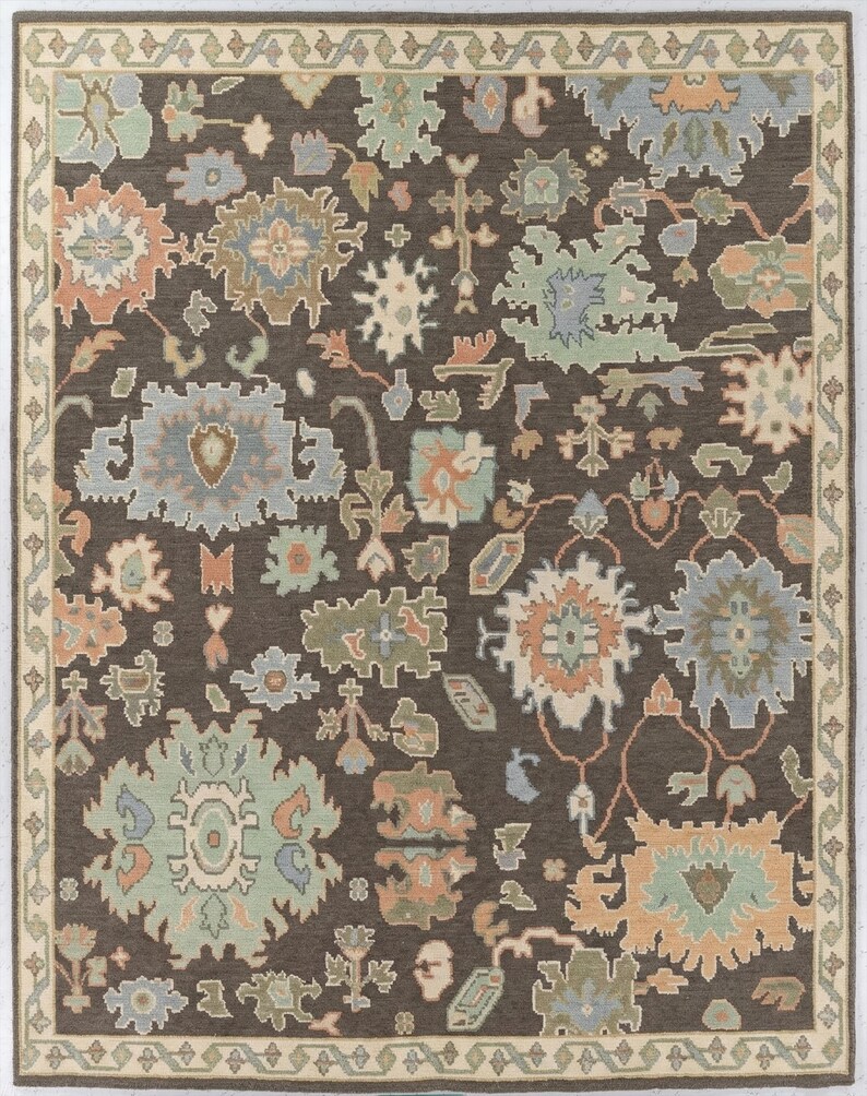 Peut inclure: Tapis rectangulaire avec un fond marron fonc&eacute; et une bordure cr&egrave;me. Le motif r&eacute;p&eacute;t&eacute; pr&eacute;sente des formes florales et g&eacute;om&eacute;triques en bleu, vert, p&ecirc;che et cr&egrave;me. Le design du tapis est complexe.