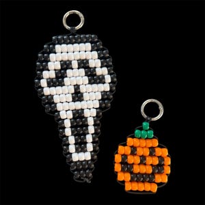 May include: Two beaded keychains featuring a ghost mask design in black and white beads and a pumpkin design in orange, black, and green beads. Each keychain is attached to a silver-toned metal ring for easy attachment to keys or bags.