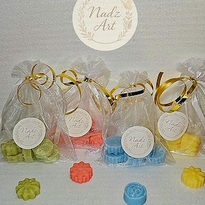 May include: Four small organza bags tied with gold ribbon, each containing colourful wax melts. The melts are green, orange, blue, and yellow, with a floral design. Each bag has a round sticker that says "Nadz Art".