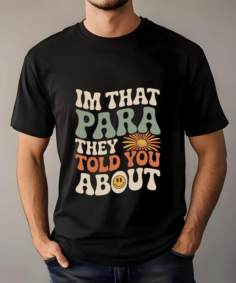K&ouml;nnte beinhalten: Schwarzes T-Shirt mit dem Text "IM THAT PARA THEY TOLD YOU ABOUT" in einem Retro-Schriftstil. Das Design beinhaltet eine G&auml;nsebl&uuml;mchen und ein Smiley-Gesicht. Das T-Shirt hat einen Rundhalsausschnitt.
