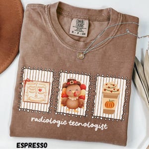 May include: A brown short-sleeve t-shirt featuring three rectangular frames with illustrations of a skeleton, a turkey wearing a hat, and a pumpkin spice coffee cup. The text "radiologic tecnologist" is printed in white below the frames.