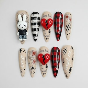 May include: A set of ten artificial nails with various designs. Designs include a sad bunny, black and white stripes, a broken heart, red and black plaid, postage stamps, and text that says "emo", "love lost", and "forget me".