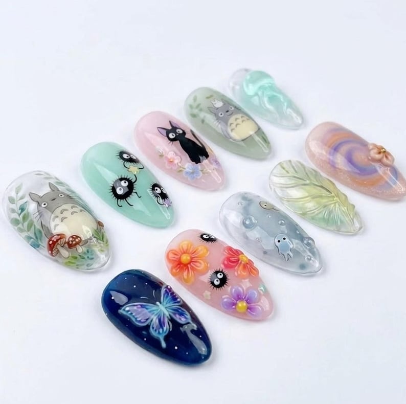 May include: A collection of ten acrylic nail designs. The nails feature various designs, including a blue butterfly, floral patterns, and cartoon characters. The color palette includes pink, blue, green, and orange.