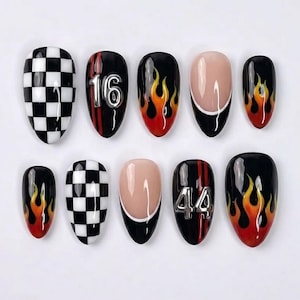 May include: A set of ten press-on nails featuring various designs including a black and white checkered pattern, red and orange flame motifs, a French tip style with a nude base, and black nails accented with metallic silver numbers 16 and 44.
