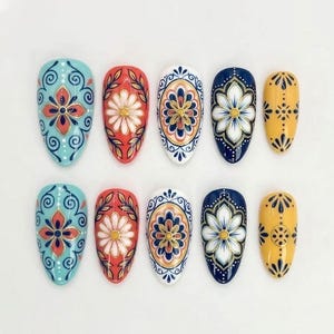 Peut inclure: Un ensemble de dix faux ongles en forme d'amande disposés sur deux rangées. Chaque ongle présente des motifs floraux et géométriques peints à la main dans des tons vifs de bleu clair, corail, blanc, bleu marine et jaune avec des détails dorés.