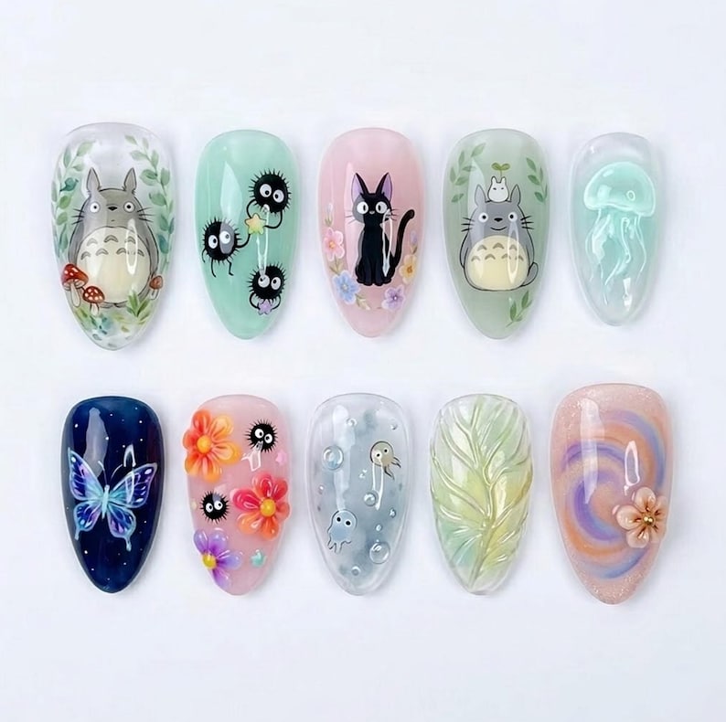 May include: A set of ten artificial nails with various designs. The designs include cartoon characters, flowers, butterflies, and abstract patterns. Colors include blue, pink, green, and white. The nails are oval-shaped and have a glossy finish.
