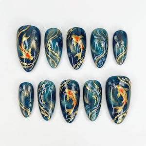 Peut inclure: Dix faux ongles en forme d'amande. Chaque ongle est peint avec une base bleu-vert foncé, des volutes dorées et un poisson koi orange vif. Le design évoque l'élégance et l'art.