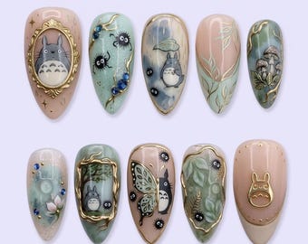 May include: A set of ten almond-shaped press-on nails featuring intricate hand-painted designs inspired by Totoro, including gold frames, soot sprites, mushrooms, butterflies, and floral motifs in shades of sage green, soft pink, and gold.