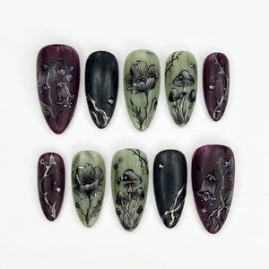 May include: A set of ten artificial nails with a dark, gothic aesthetic. The nails feature hand-painted designs of flowers, mushrooms, and vines in shades of black, green, and purple. Some nails have a glossy finish, while others are matte.