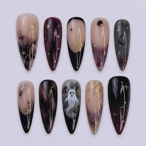 May include: Ten almond-shaped press-on nails featuring a dark color palette of black and deep purple with glossy finishes. Designs include gold foil star accents, intricate spider web patterns, a white ghost illustration, and a crescent moon.