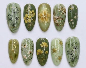 May include: A set of ten artificial nails with a green marble effect. Each nail features a different floral design in gold and white, including detailed flower and leaf patterns. The nails are oval-shaped and showcase various shades of green.