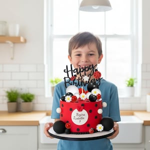 Può includere: Una torta di compleanno rossa con pois neri, decorata con dettagli bianchi e neri, margherite e dettagli di coccinelle. La torta ha un topper nero "Happy Birthday" e un cerchio bianco con il nome "Regina Isabella" e il numero "7".