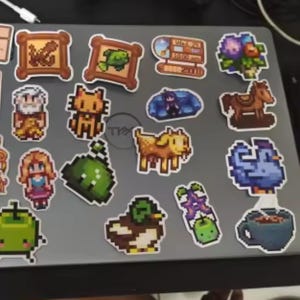 Peut inclure: Une collection d'autocollants pixel art repr&eacute;sentant divers personnages et objets. Comprend un poisson encadr&eacute;, un chat, une ch&egrave;vre, un canard, un cheval, un oiseau bleu, une tasse de caf&eacute; et une horloge indiquant "Wed 21 10:00 am".