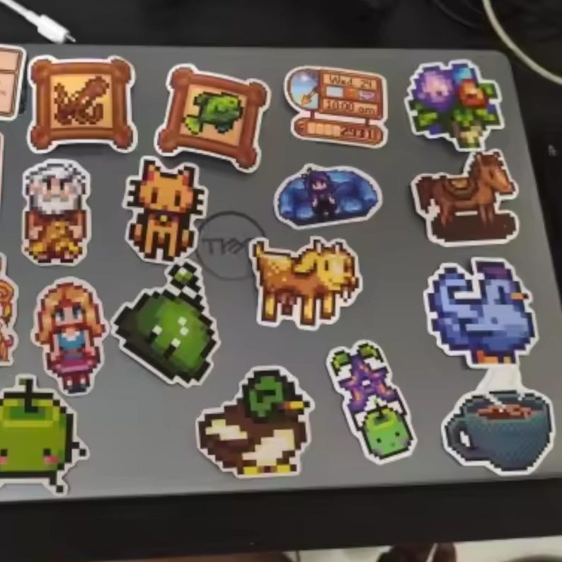 Peut inclure: Une collection d'autocollants pixel art repr&eacute;sentant divers personnages et objets. Comprend un poisson encadr&eacute;, un chat, une ch&egrave;vre, un canard, un cheval, un oiseau bleu, une tasse de caf&eacute; et une horloge indiquant "Wed 21 10:00 am".