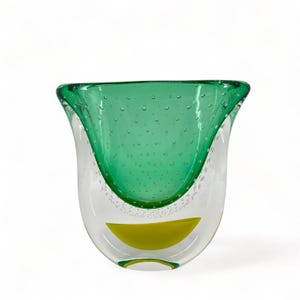 May include: A clear glass vase with a green interior and a yellow accent at the base. The green section has small air bubbles. The vase has a distinctive, curved form.