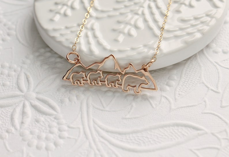 Op de afbeelding: Een gouden ketting met een hanger met een silhouet van een bergketen met vier beren die er voor lopen.