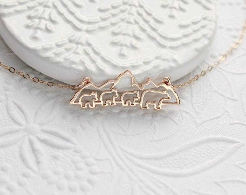 Op de afbeelding: Een gouden ketting met een hanger met een silhouet van een bergketen met vijf beren die er voor lopen.