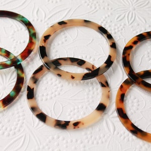 Op de afbeelding: Vijf ronde, schildpad-gepatroneerde plastic armbanden in verschillende tinten bruin, zwart en cr&egrave;me. De armbanden zijn op elkaar gestapeld.