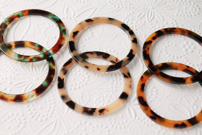 Op de afbeelding: Vijf ronde, schildpad-gepatroneerde plastic armbanden in verschillende tinten bruin, zwart en cr&egrave;me. De armbanden zijn op elkaar gestapeld.
