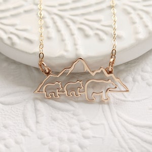 Op de afbeelding: Gouden ketting met een hanger met een silhouet van drie beren die voor een bergketen lopen.