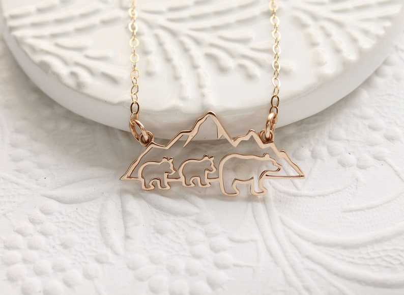 Op de afbeelding: Gouden ketting met een hanger met een silhouet van drie beren die voor een bergketen lopen.