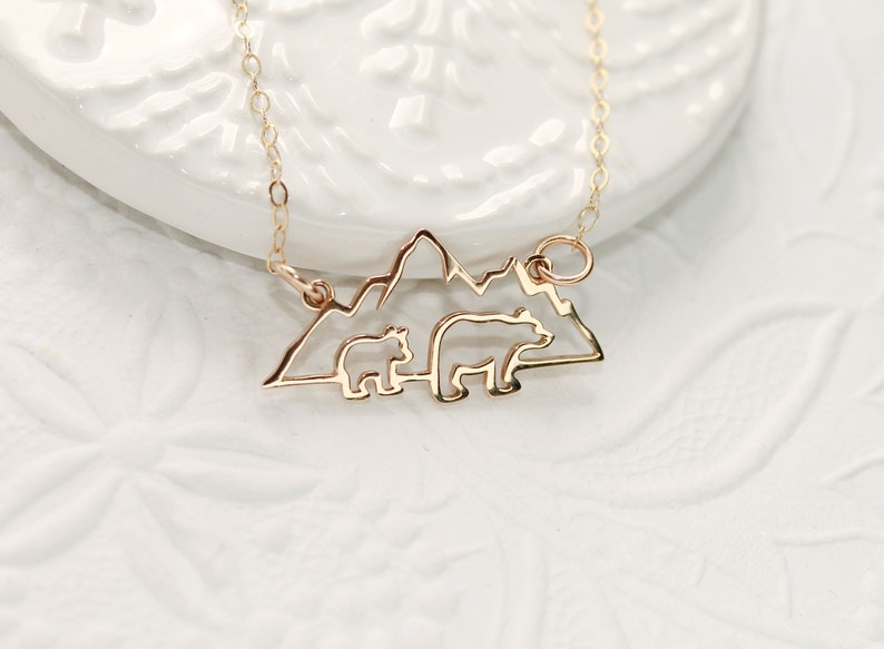 Op de afbeelding: Gouden ketting met een hanger met een silhouet van een bergketen met twee beren erin. De beren kijken in dezelfde richting, met de grotere beer voor de kleinere beer.