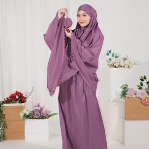May include: A solid mauve prayer garment consisting of a long, loose-fitting hooded top with wide sleeves and a matching floor-length skirt. The top features a scalloped edge along the sleeve opening and is held with a small matching pouch.